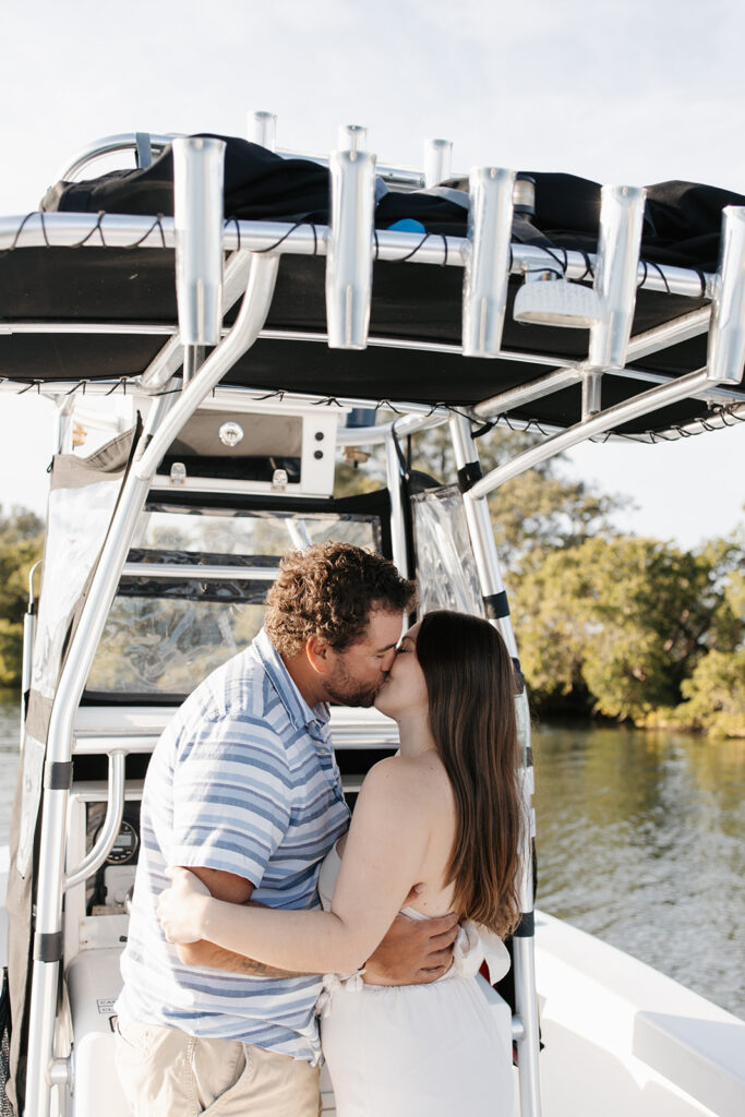 man and woman share a kiss during their boat engagement photoshoot