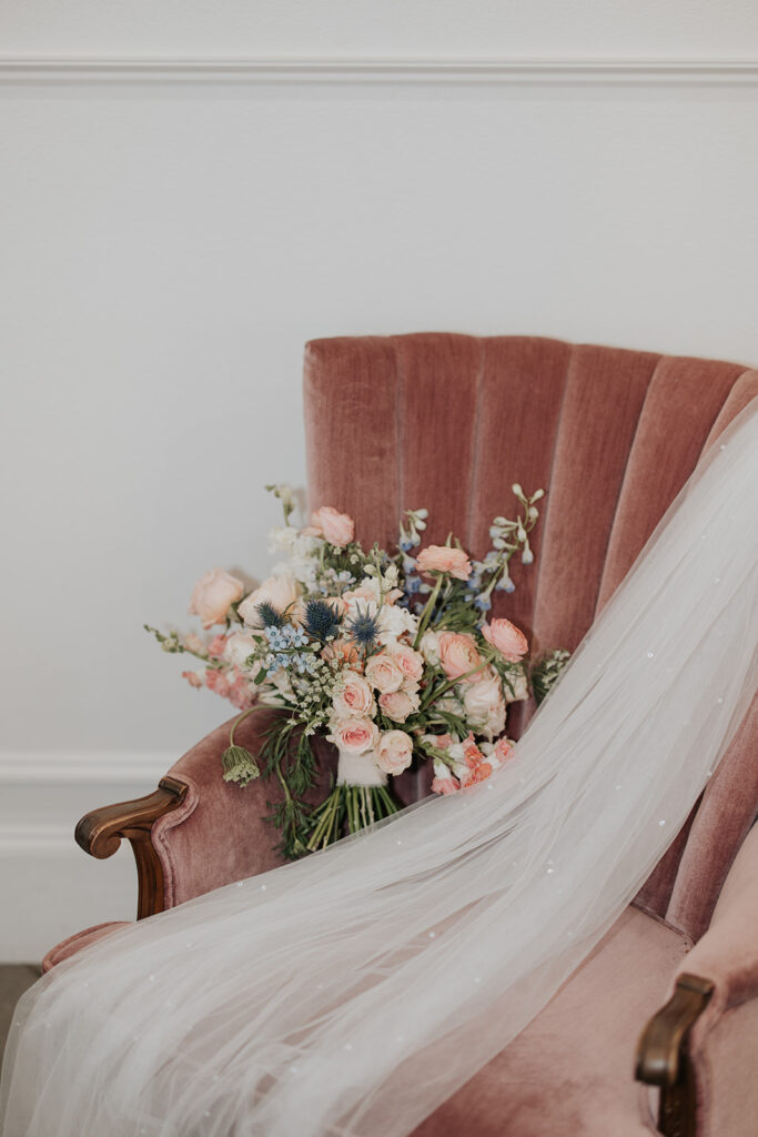 wedding bouquet sitting beside veil on a pink velvet chair