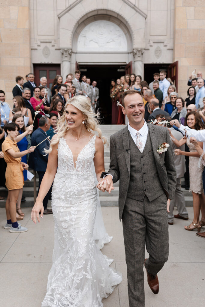 bride and groom cheerfully walk out of the Catholic church after their wedding ceremony