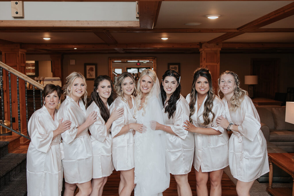 bride and her bridesmaids stand together in their silk robes before wedding ceremony