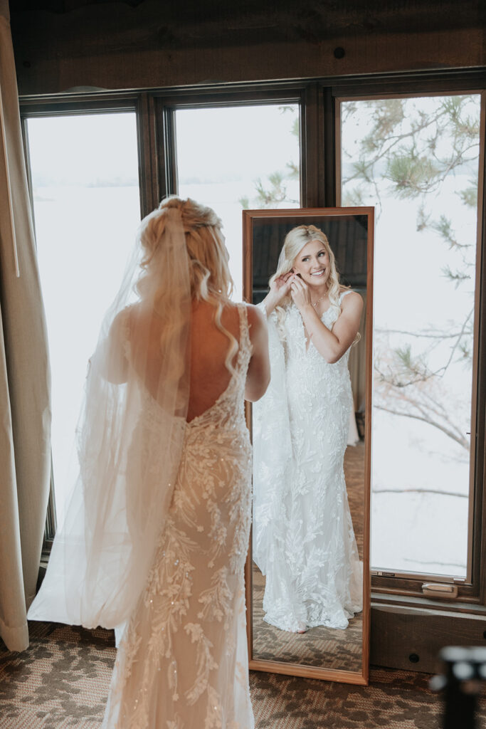 bride stands in front of mirror while putting in earrings