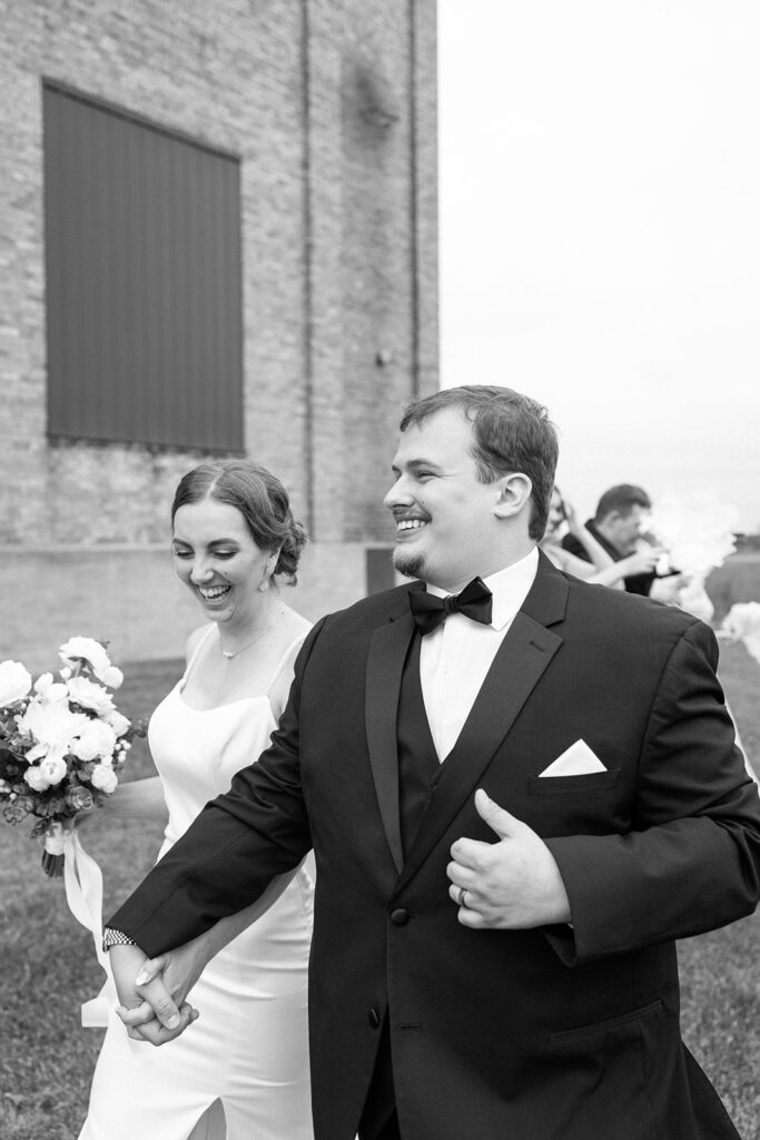 Bride and groom walk hand in hand with big grins
