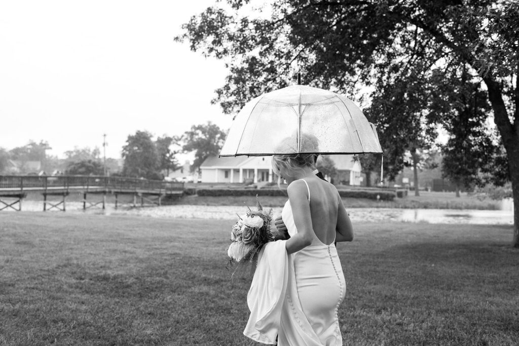 Bride walks as she holds a clear umbrella and then end of her wedding gown.