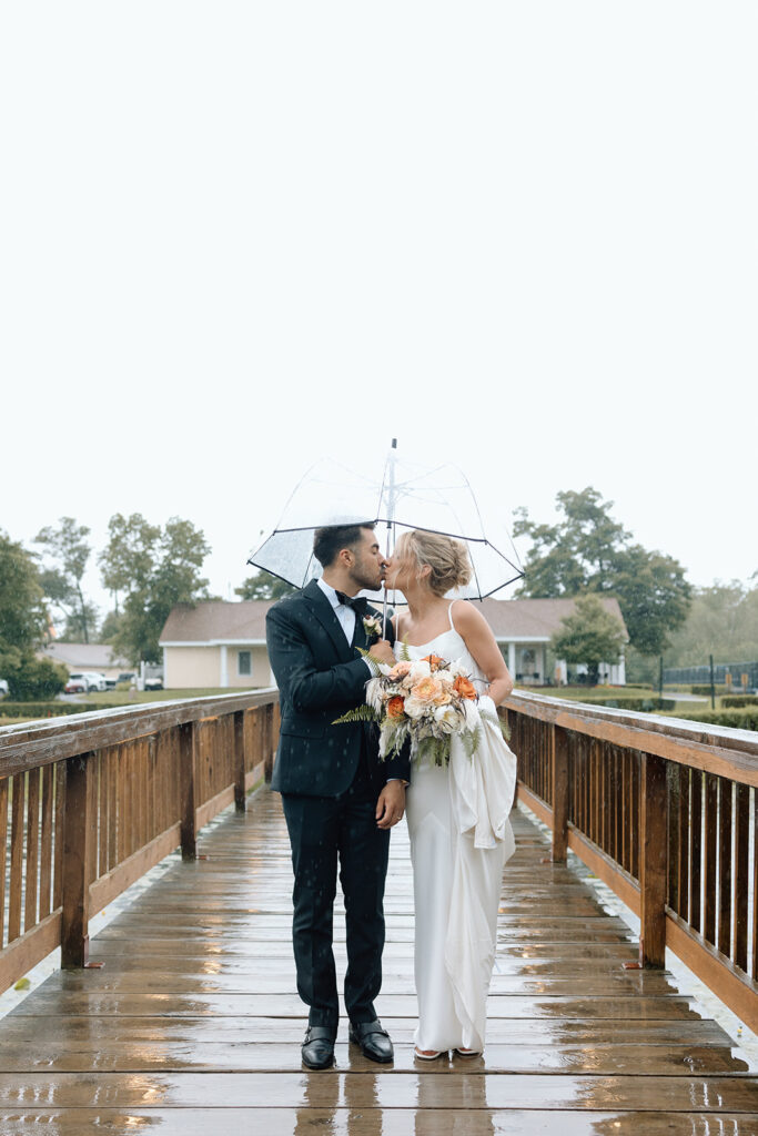 Bride and groom standing in the rain with their clear umbrella