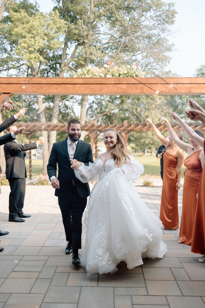 bride and groom walking through their wedding party holding sparklers