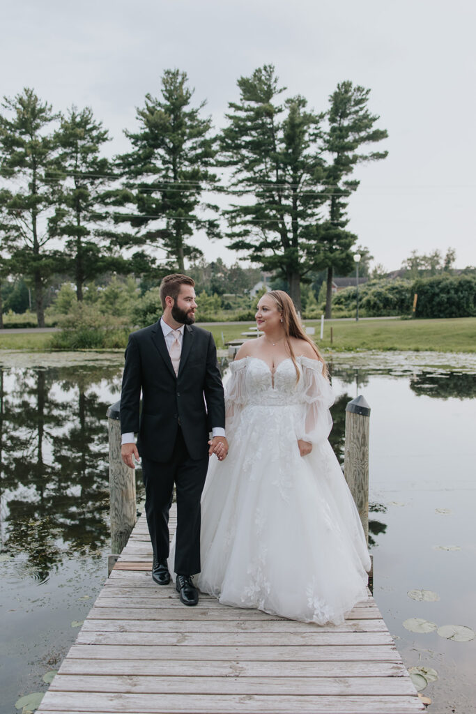 Bride and groom stand on a dock on a pond with lily pads