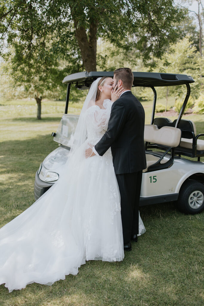 Bride and groom kissing by a golf cart