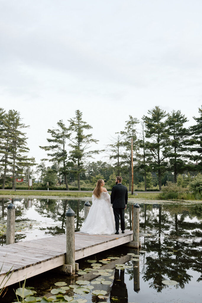 Bride and groom stand on a dock on a pond with lily pads