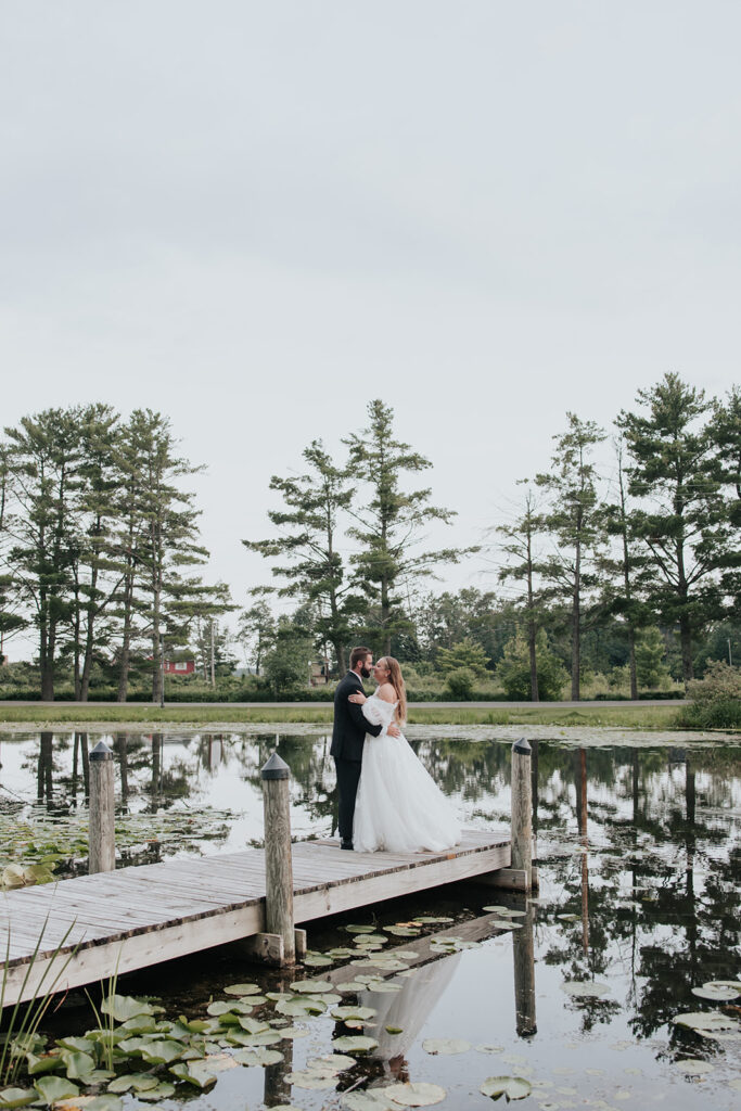 Bride and groom stand on a dock on a pond with lily pads