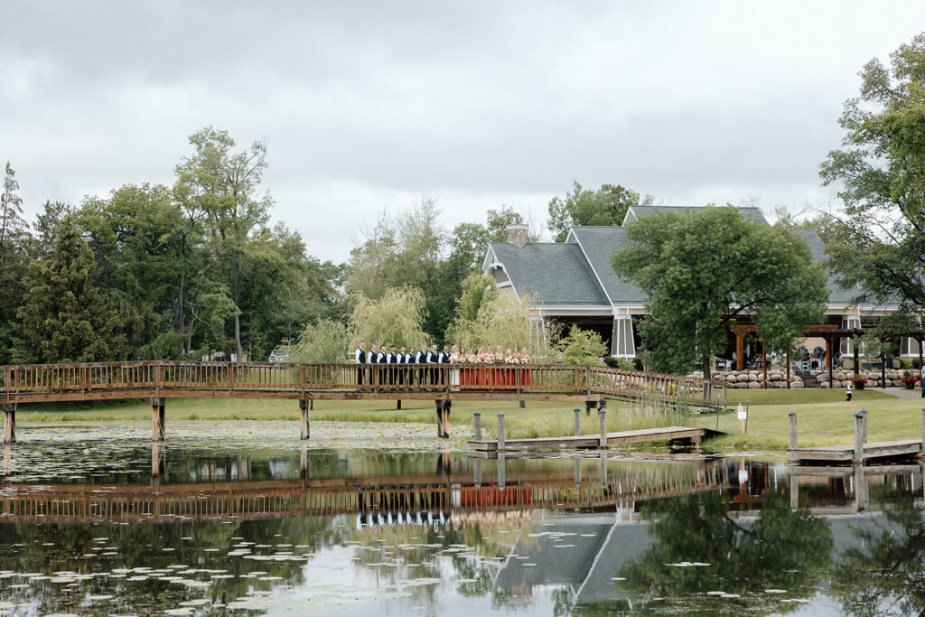 Bride and groom stand with their wedding party on a wooden bridge over the lake at madden's on gull lake wedding reception