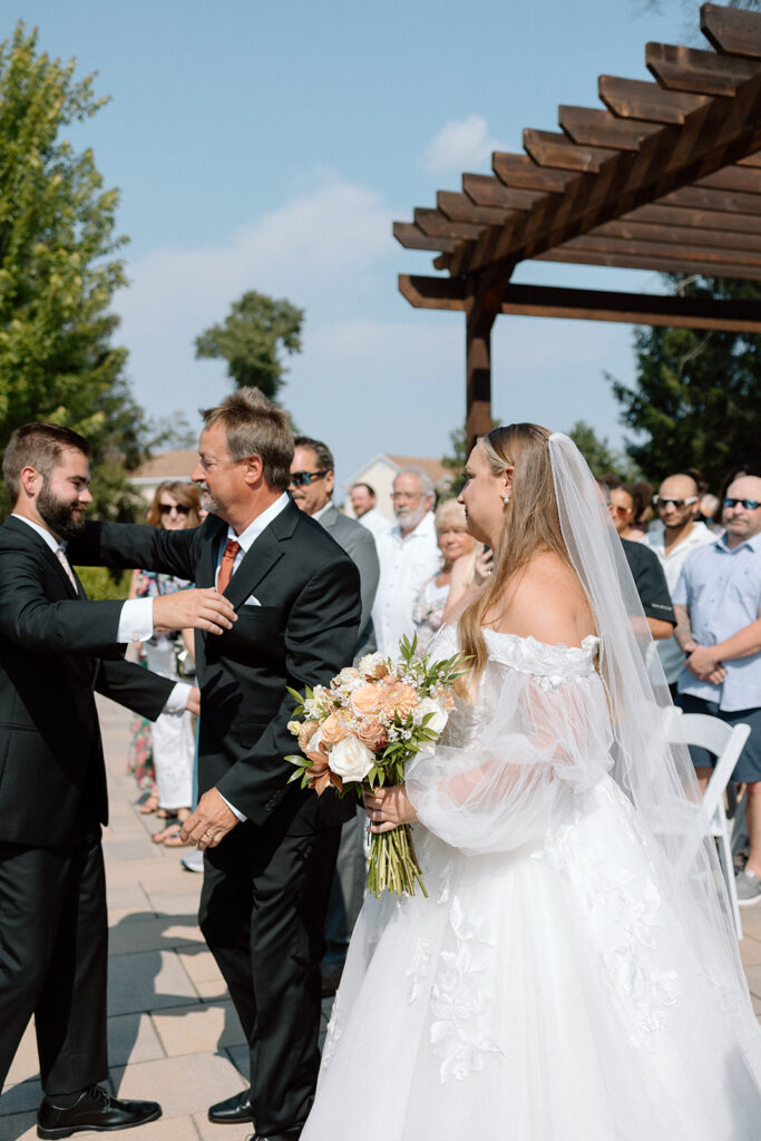 father hugging groom as he hands off the bride