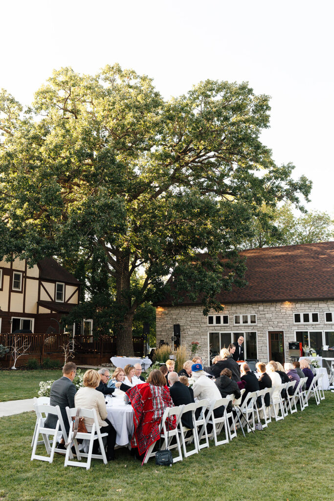 Guests enjoying the outdoor reception under the large tree with hanging lights
