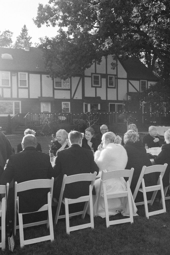Guests enjoying the outdoor reception under the large tree with hanging lights
