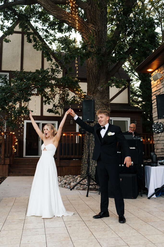 Guests enjoying the outdoor reception under the large tree with hanging lights
