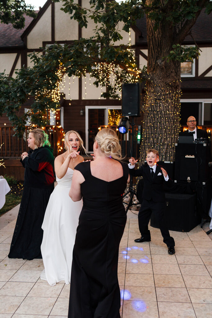 Guests enjoying the outdoor reception under the large tree with hanging lights
