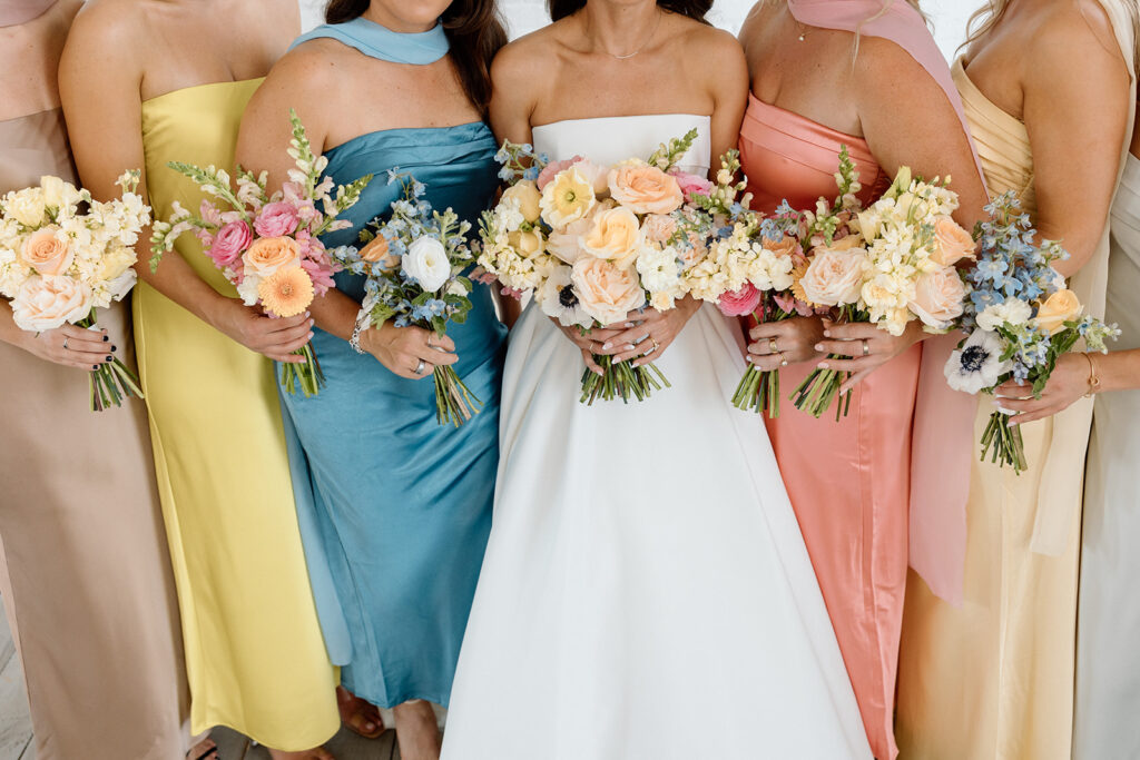 Bridesmaids in colorful dresses holding vibrant bouquets by Bloom Designs
